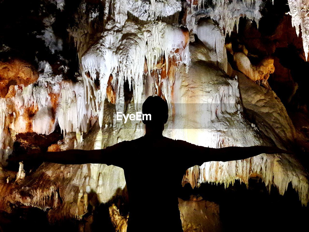 Silhouette man with arms outstretched in cave