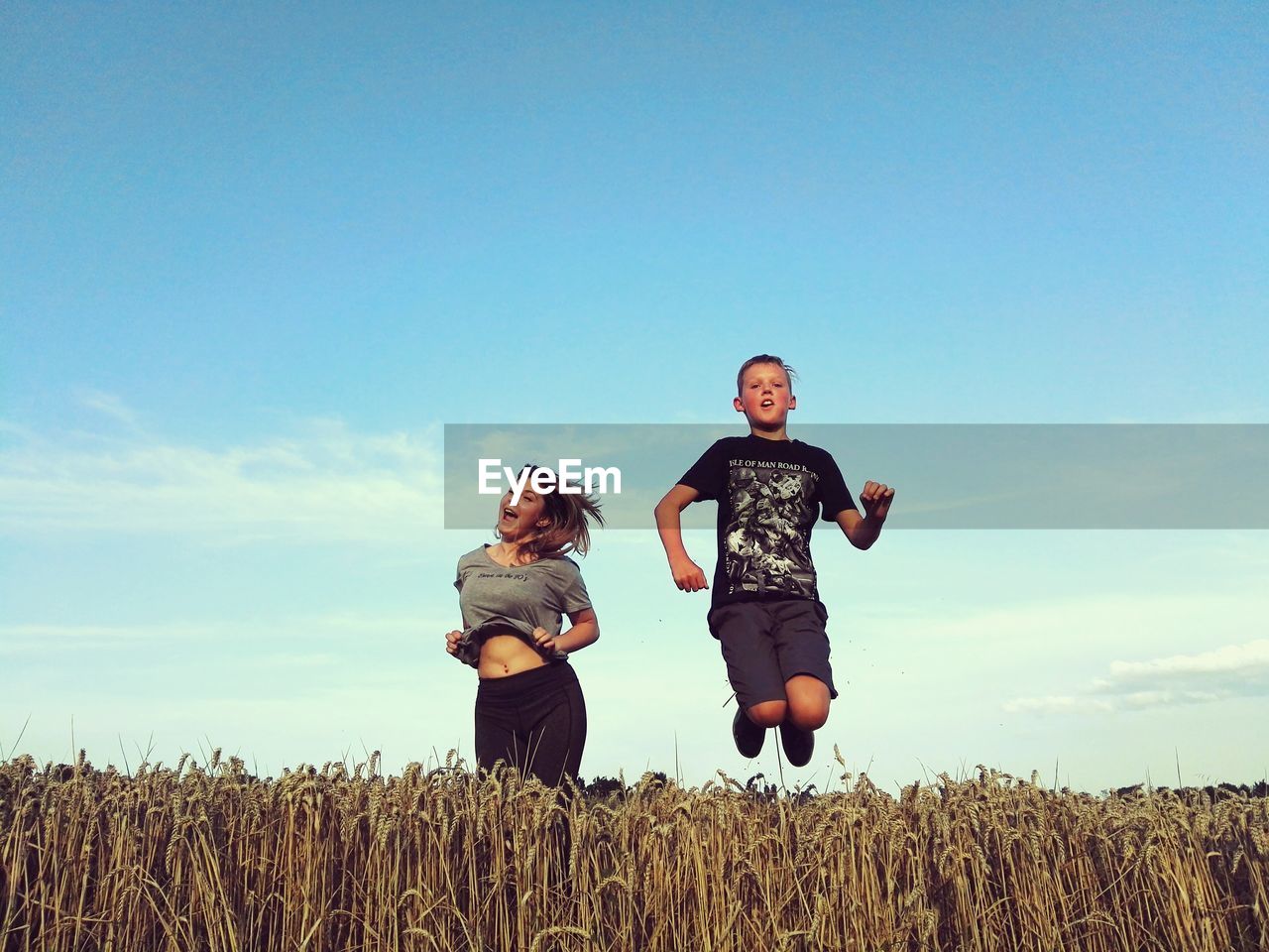 Teenage friends jumping amidst cereal plants against sky at agricultural field