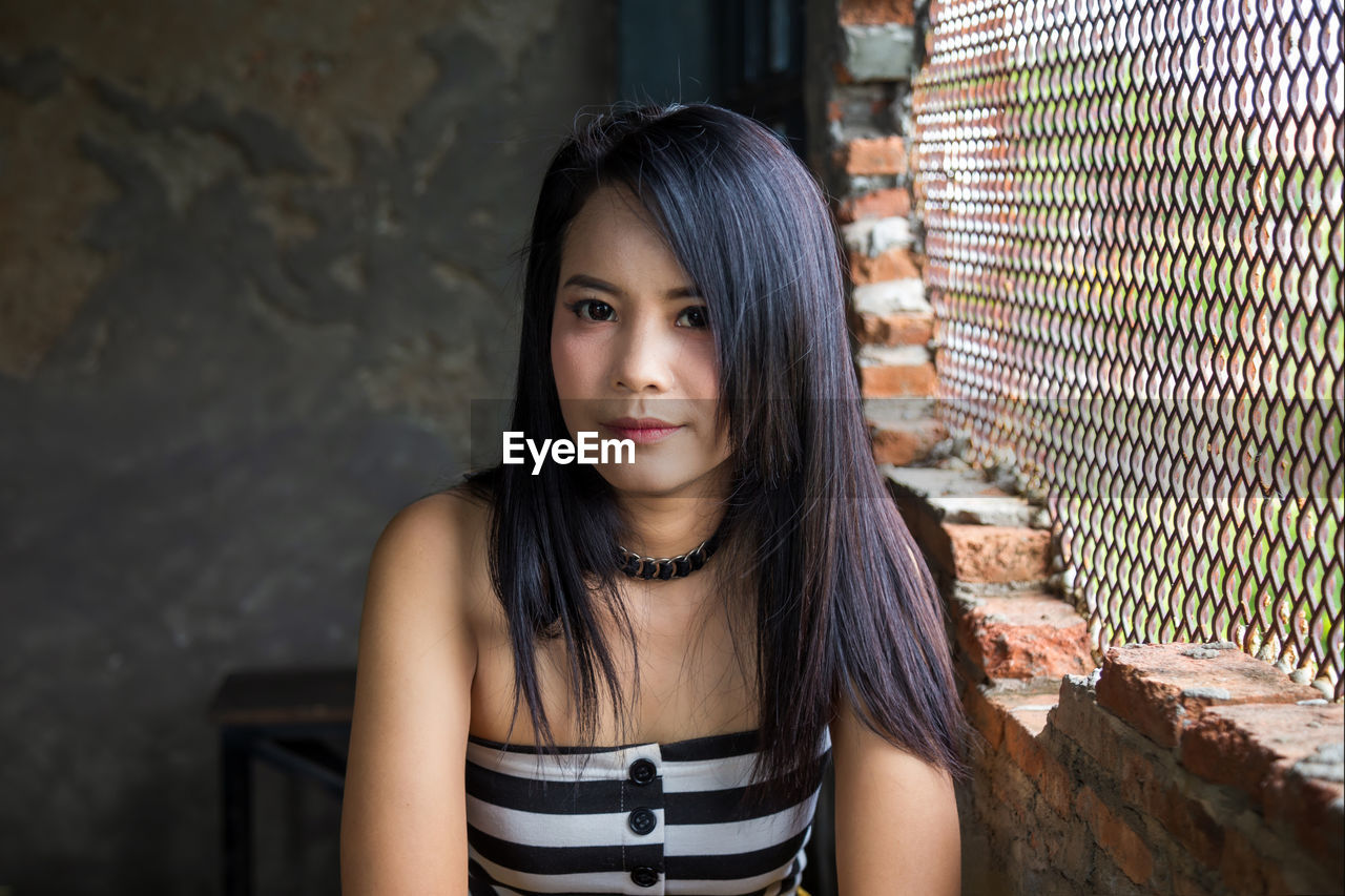 Portrait asian woman lookinging at a camera next to brick wall.