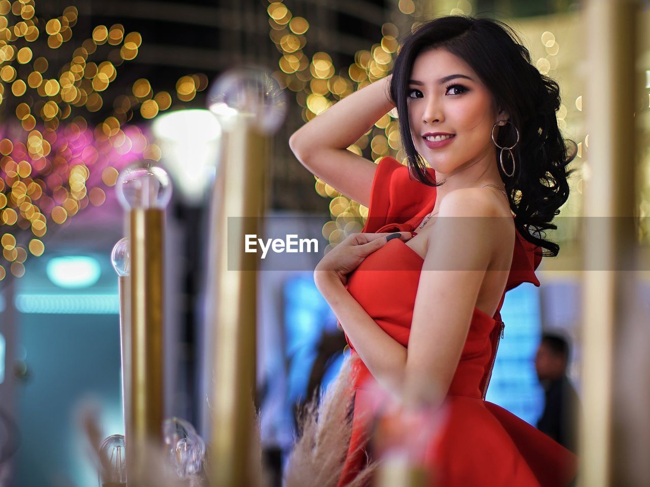 Portrait of smiling woman standing against illuminated lighting equipment outdoors