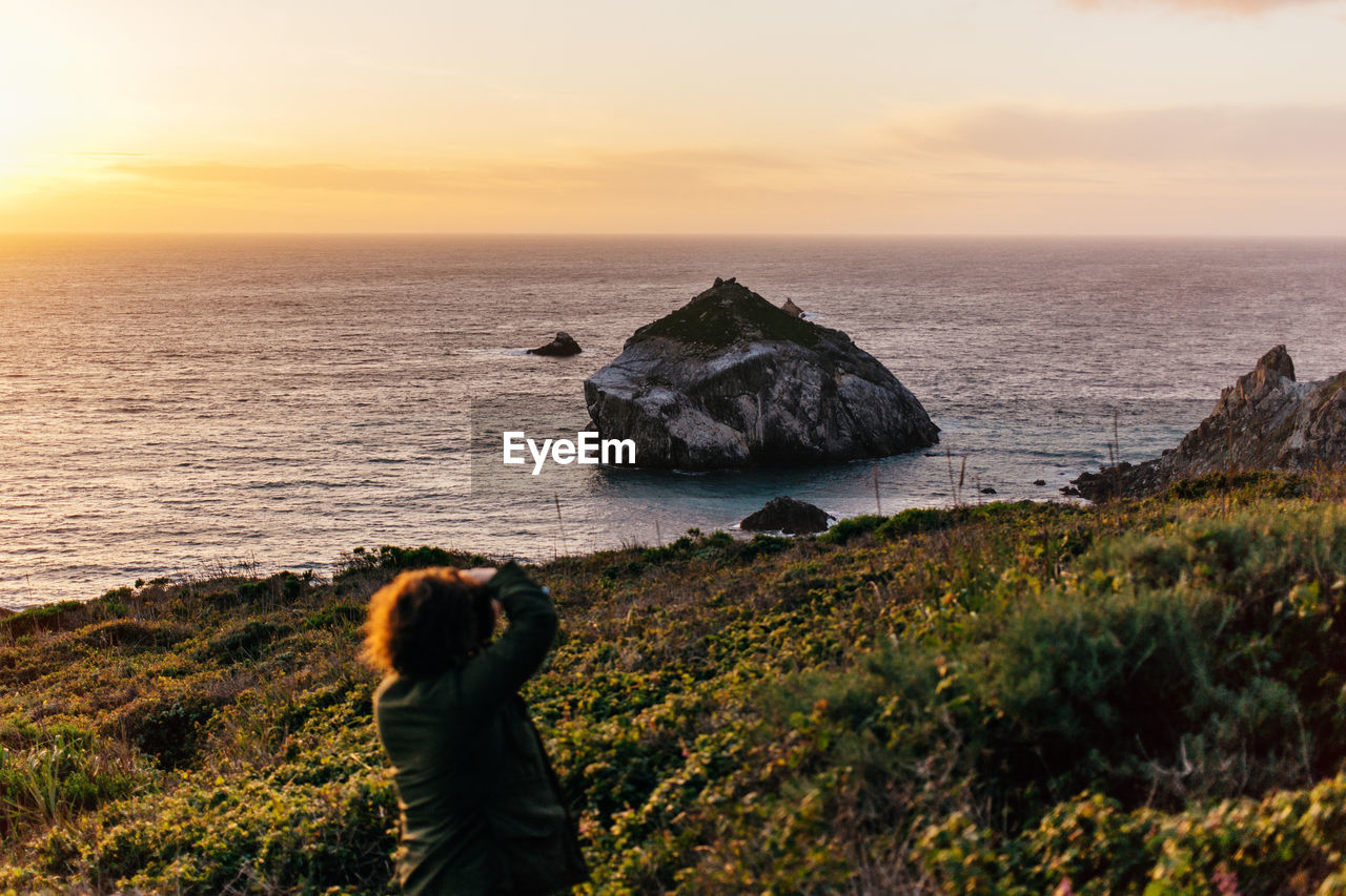 Woman standing on rock by sea against sky during sunset