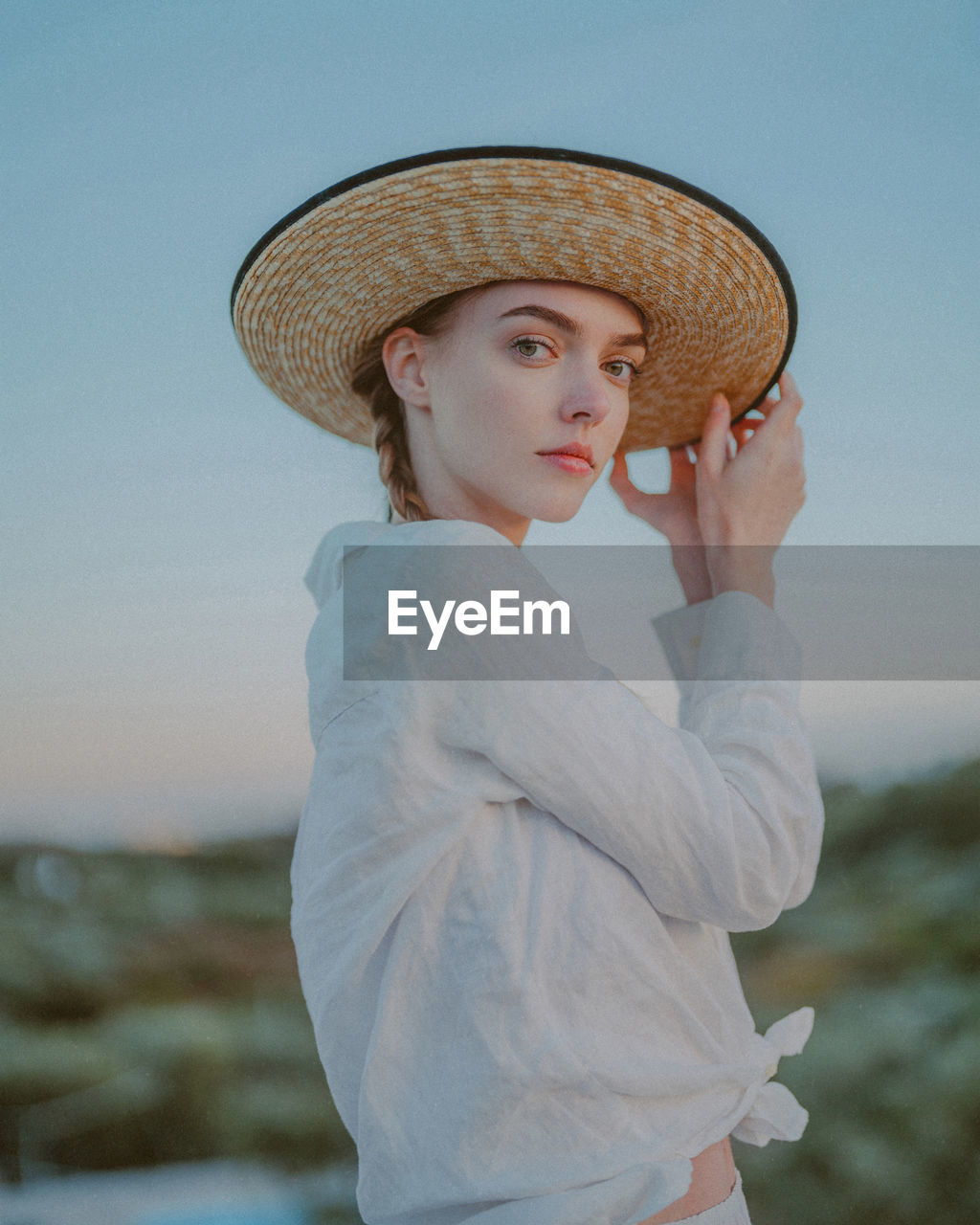 PORTRAIT OF YOUNG WOMAN WEARING HAT AGAINST SKY