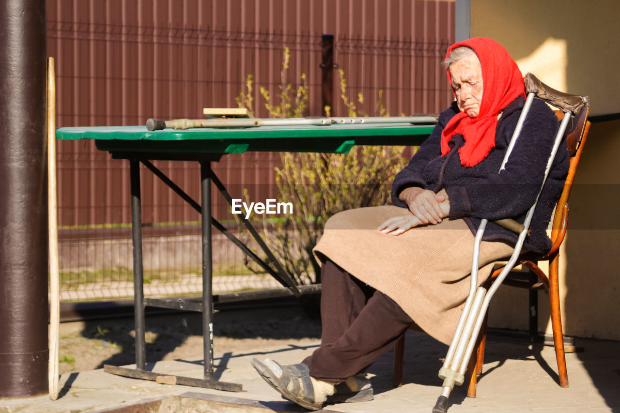 Ukrainian elderly woman in red shawl sleeping outside. 90 years old. alone person. sick and homecare