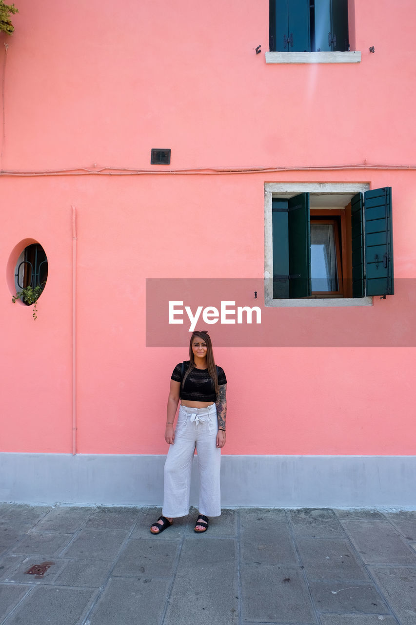 Full length portrait of smiling woman standing against building