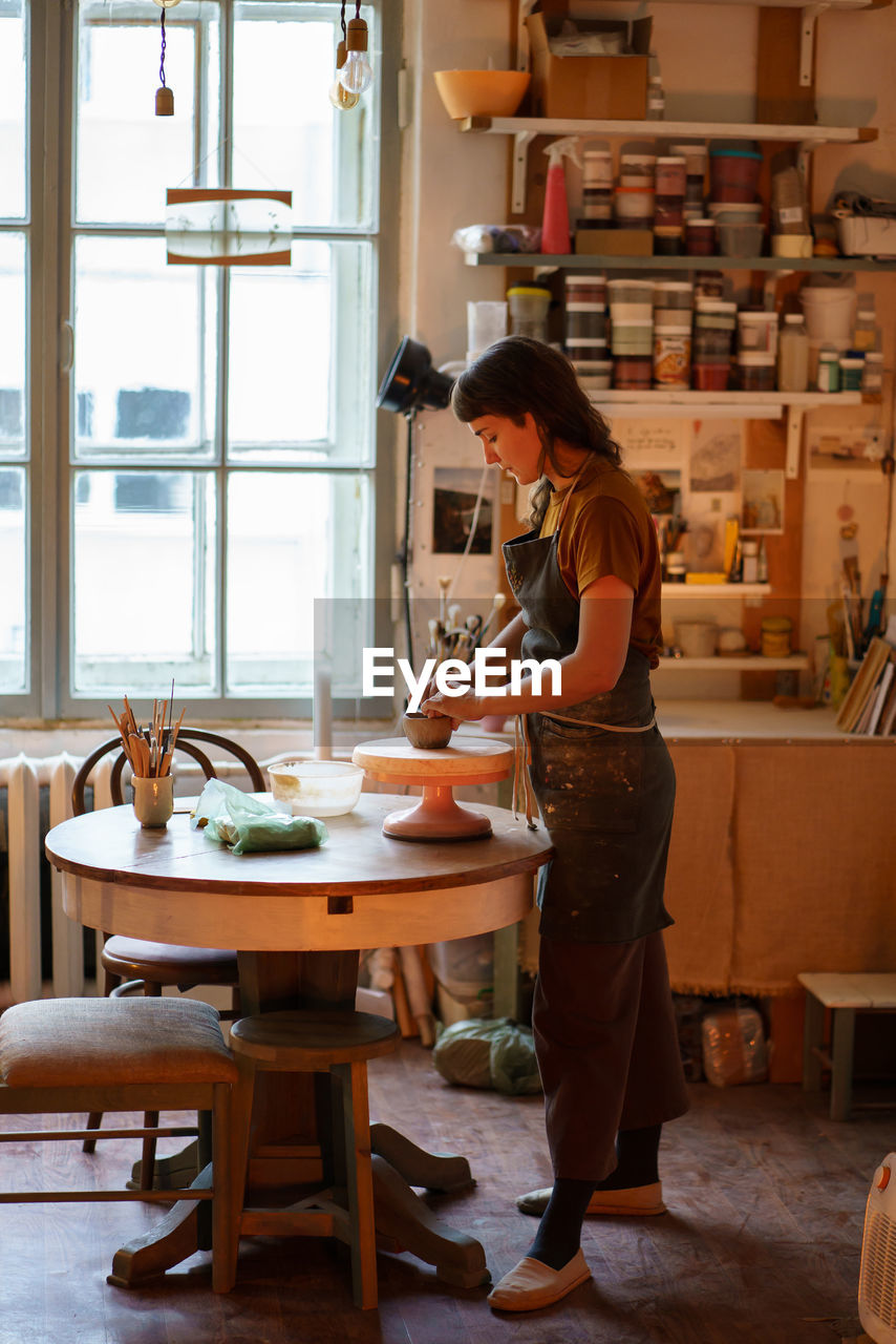 Young female potter maker work with clay on pottery wheel in creative space or professional studio