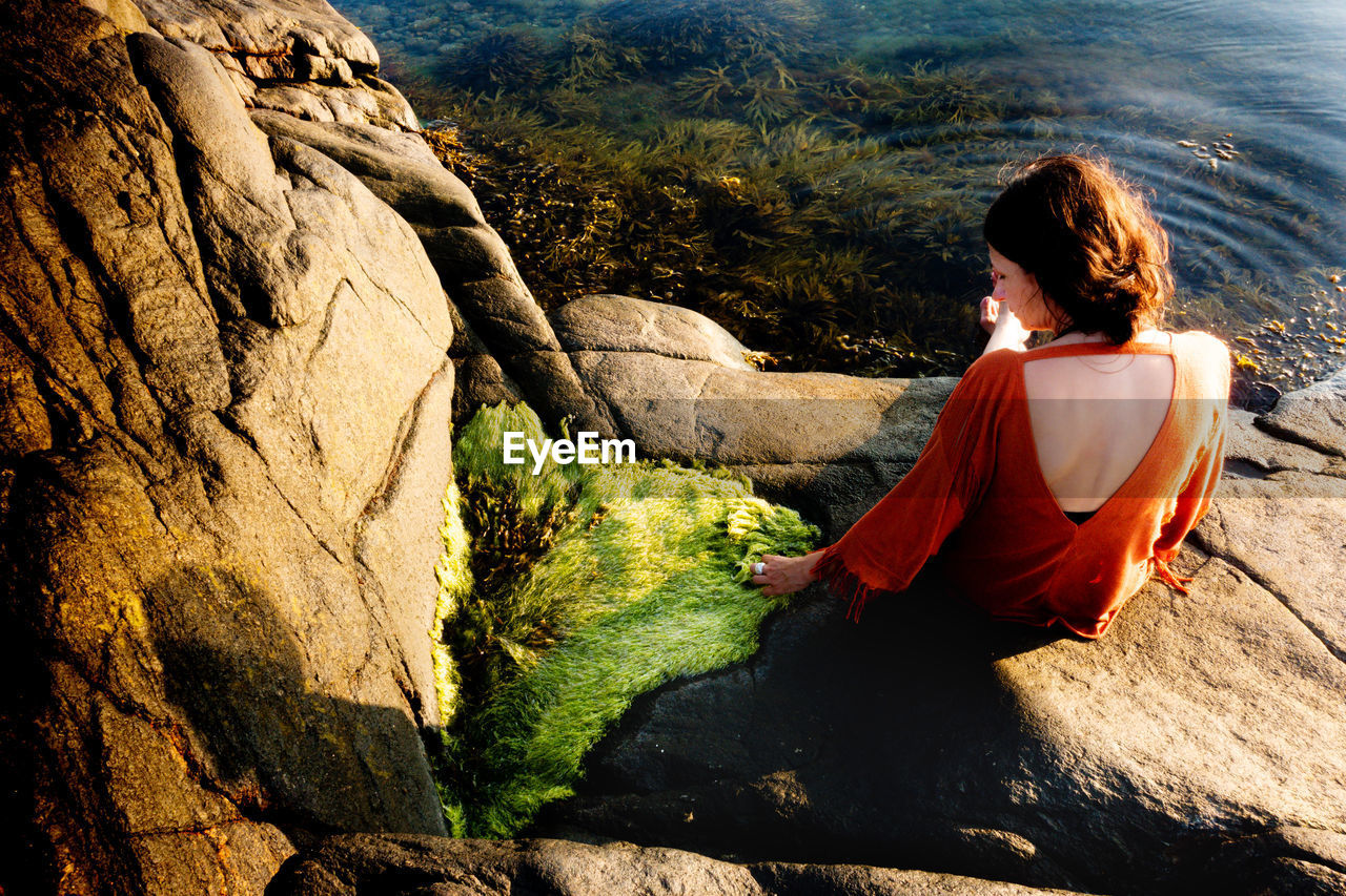 Rear view of woman sitting on rock at beach