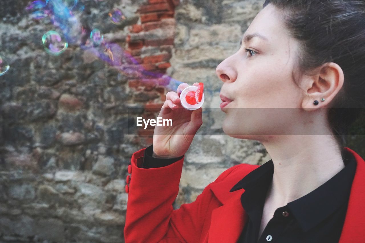 Close-up of young woman blowing bubbles against wall