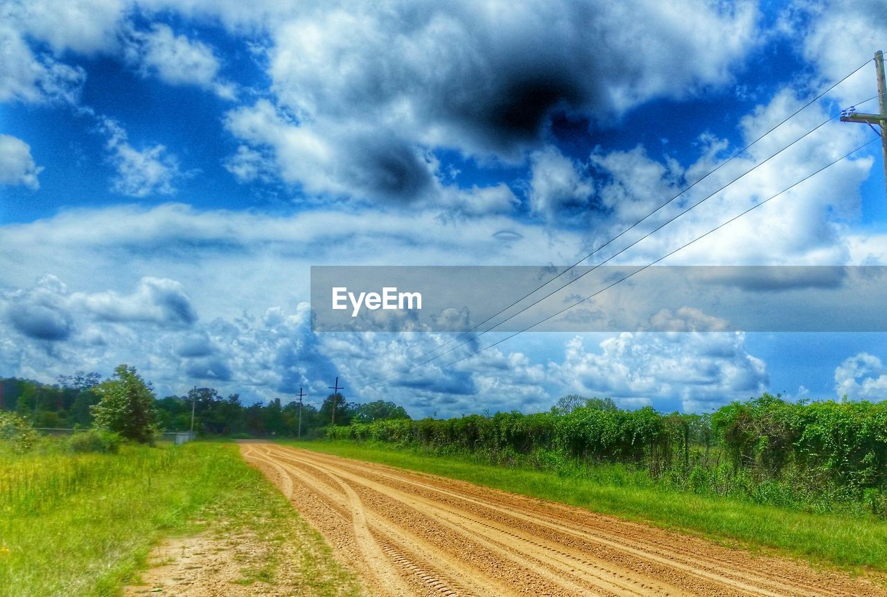 Scenic view of street by field against cloudy sky