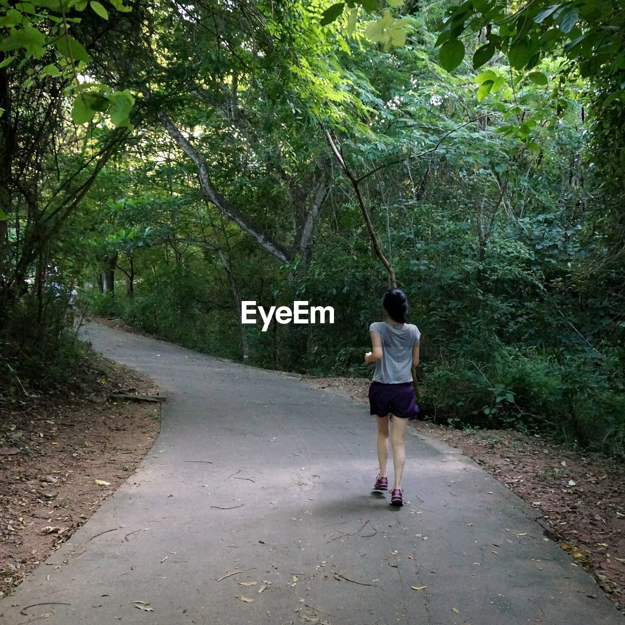 Rear view of young woman jogging on road in forest