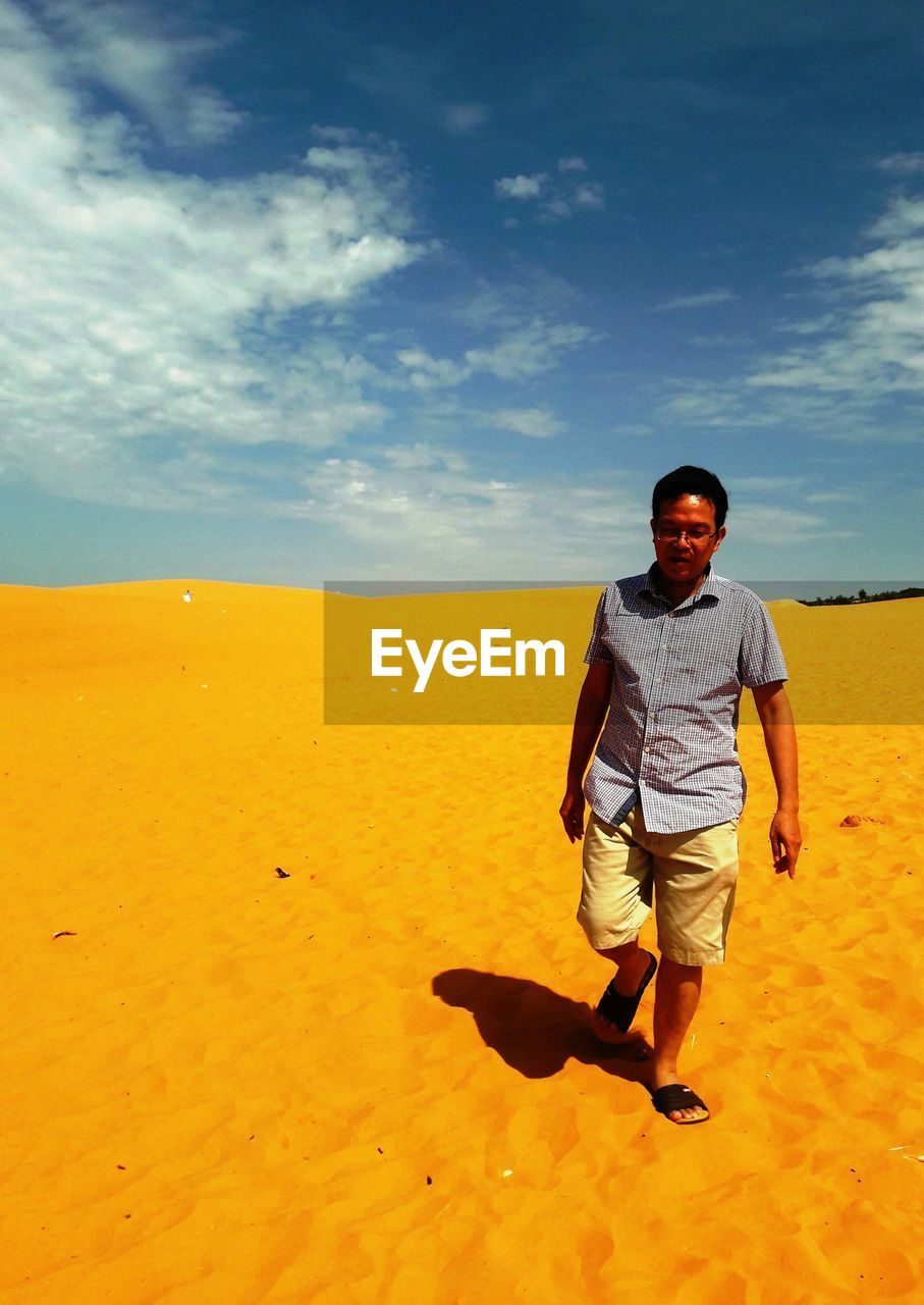 Full length of man walking on sand against cloudy sky