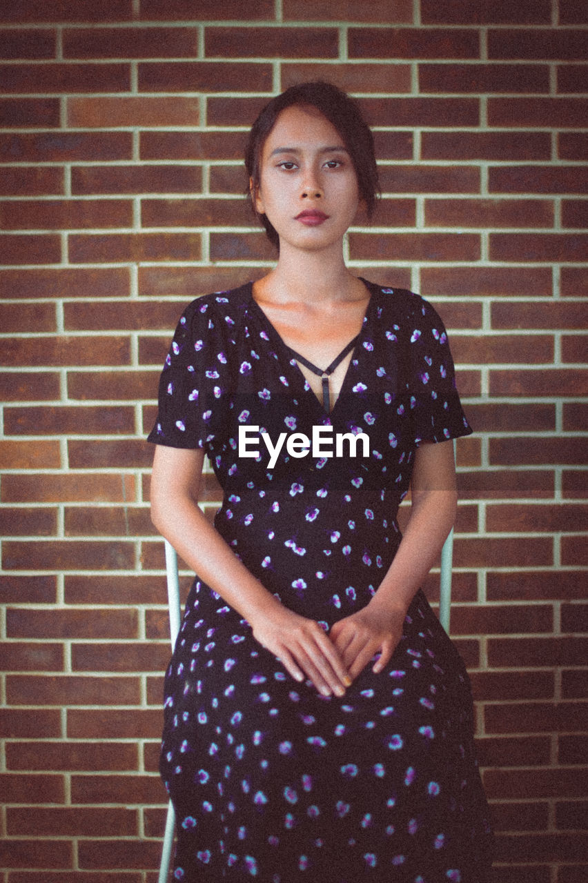 Portrait of woman sitting against brick wall