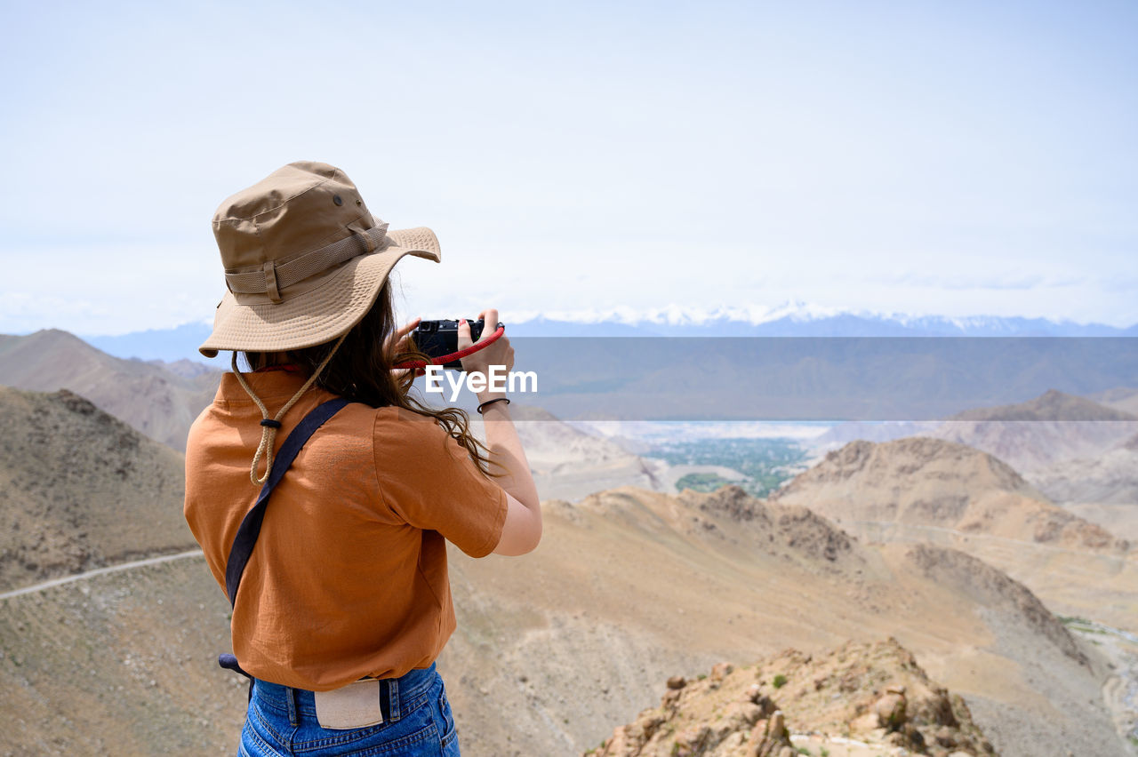 REAR VIEW OF PERSON PHOTOGRAPHING CAMERA ON LAND