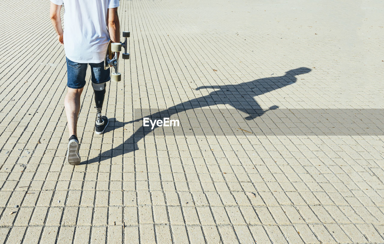 Young man with leg prosthesis walking and holding skateboard