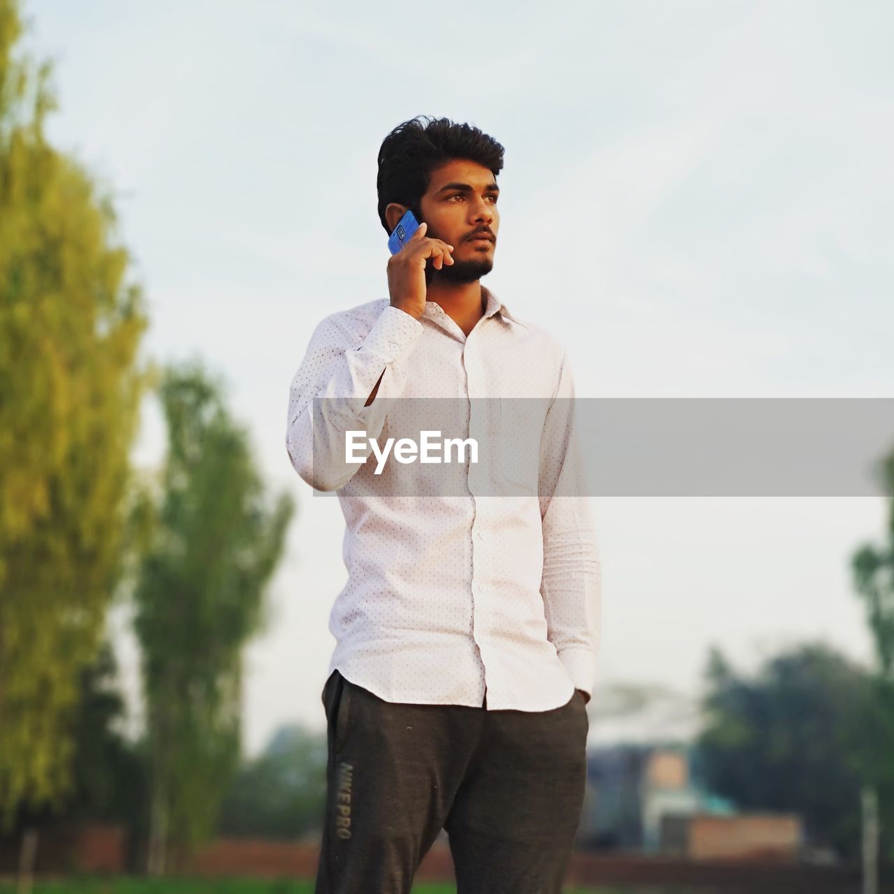 YOUNG MAN USING MOBILE PHONE STANDING AGAINST SKY