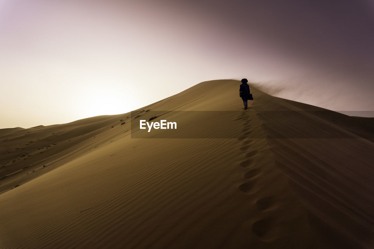 Man standing on sand dune in desert against clear sky