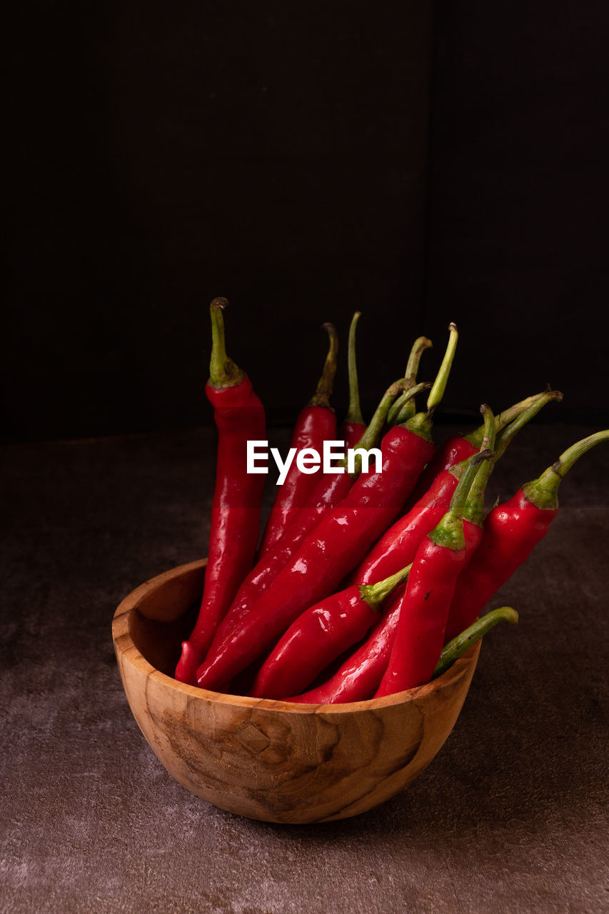 CLOSE-UP OF CHILI PEPPERS ON TABLE AGAINST BLACK BACKGROUND