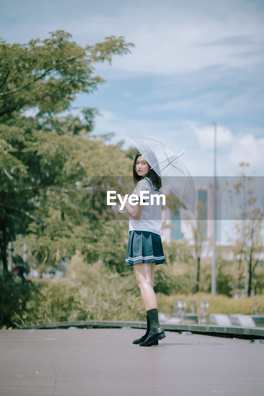 Portrait of young woman with umbrella standing on footpath