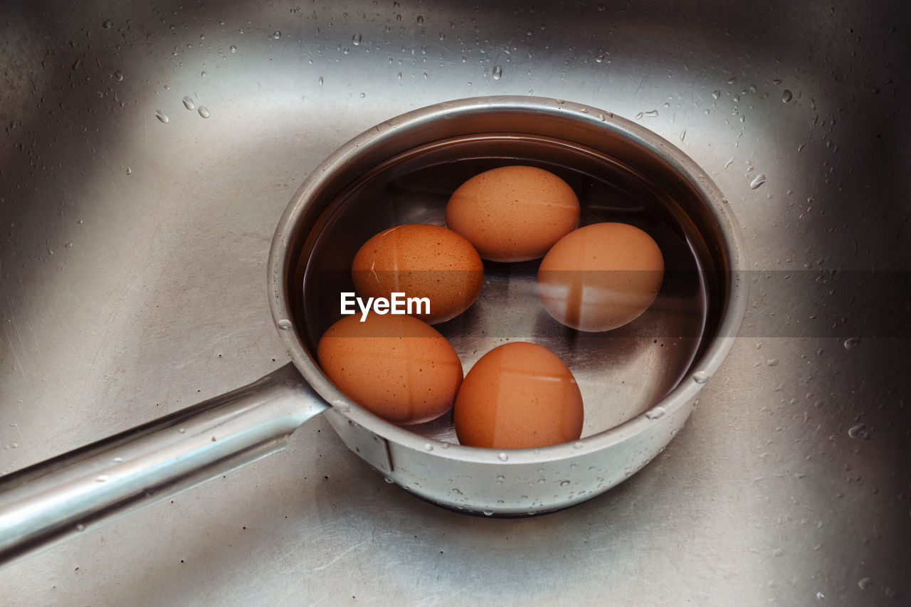 Boiled chicken eggs lie in a ladle with cold water