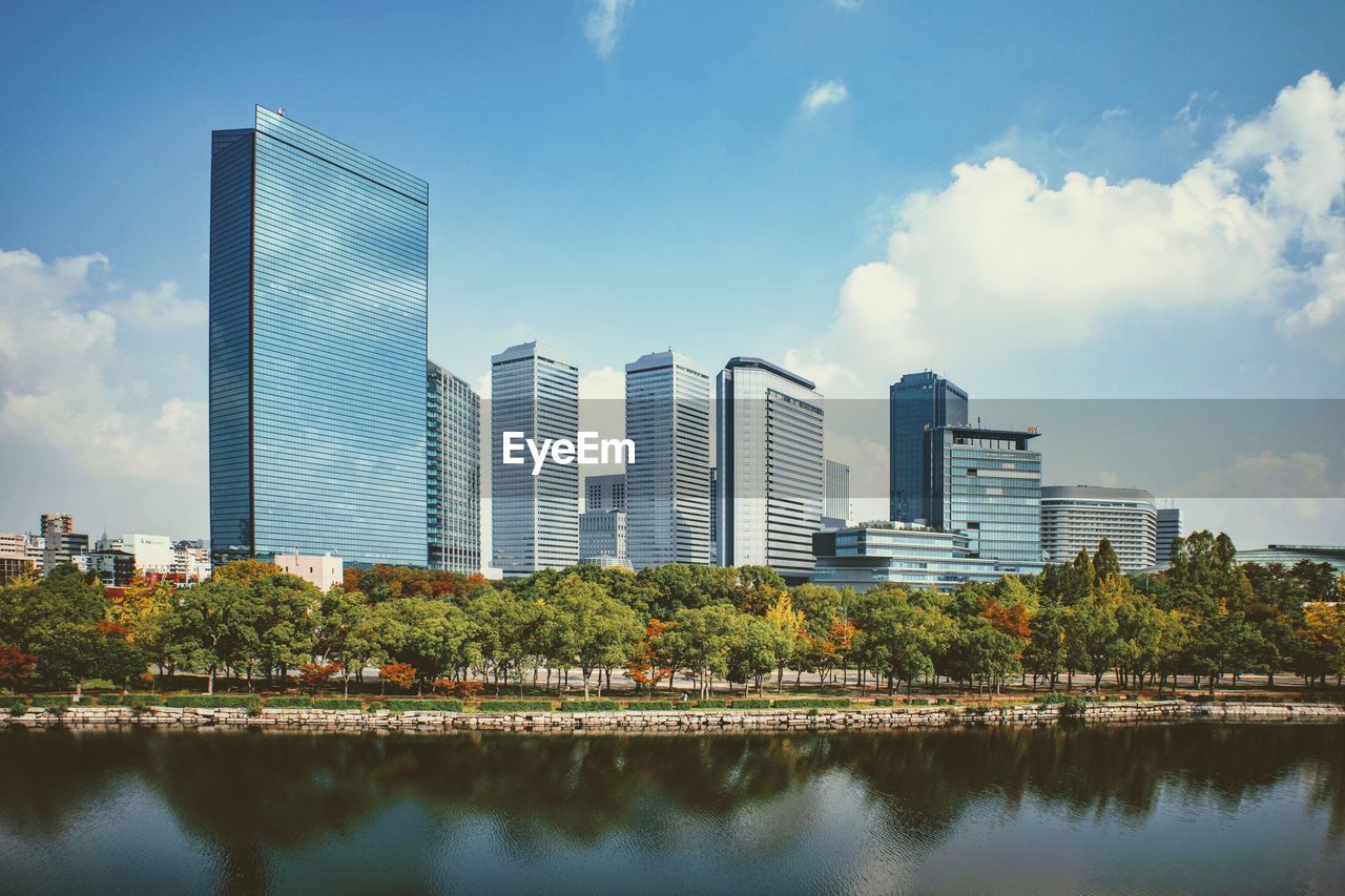 Reflection of trees and buildings in city against sky