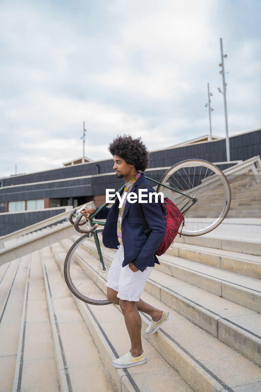 Stylish man carrying bicycle on stairs in the city