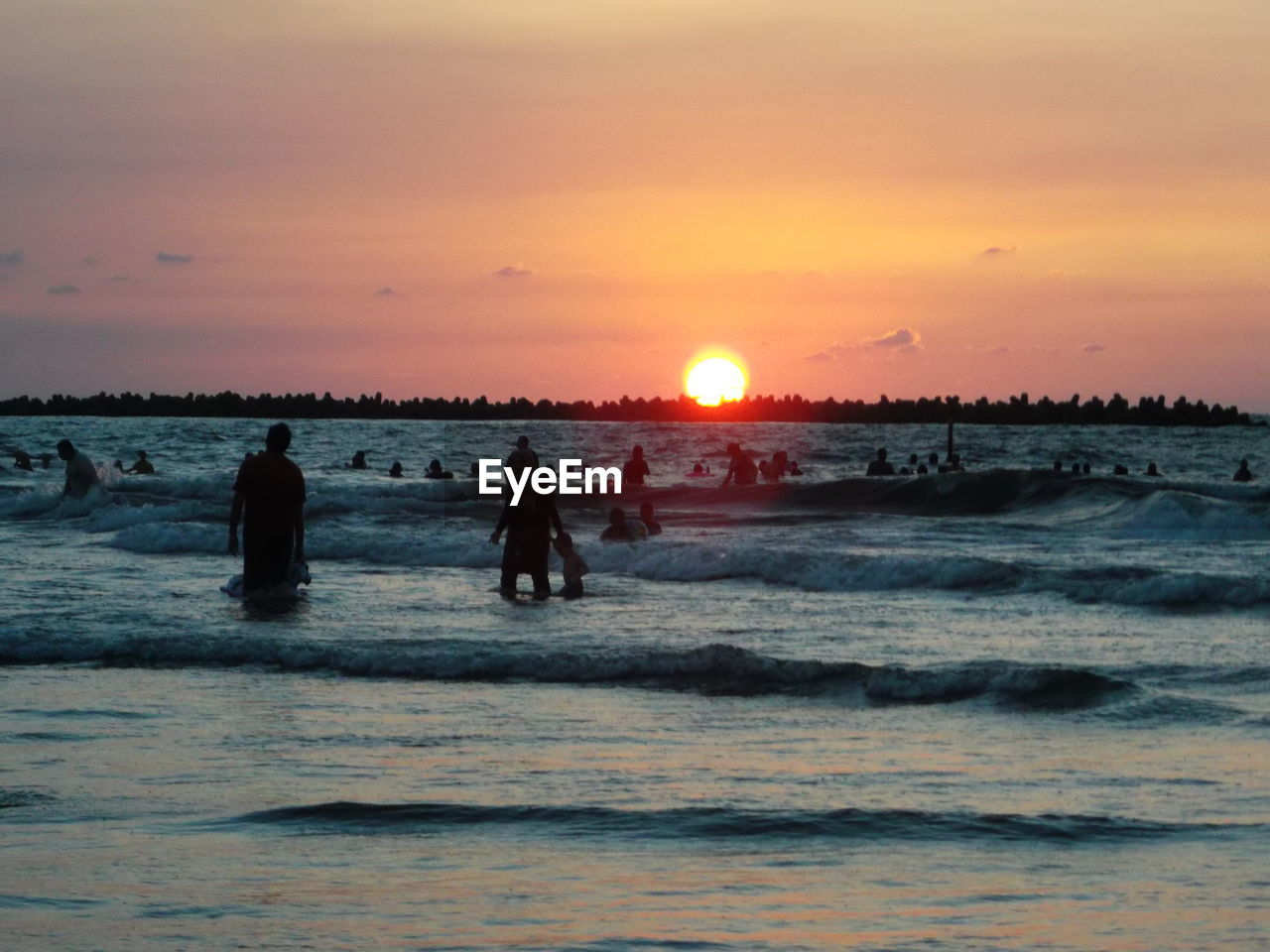 Silhouette people in sea against sky during sunset