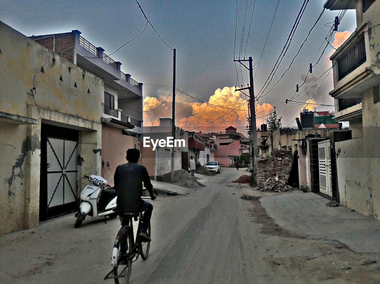 REAR VIEW OF MAN RIDING BICYCLE ON ROAD AGAINST SKY