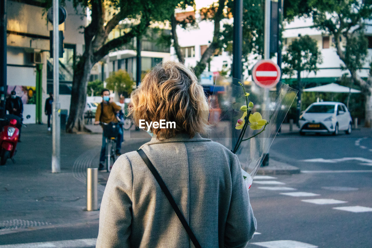 REAR VIEW OF WOMAN ON CITY STREET BY ROAD