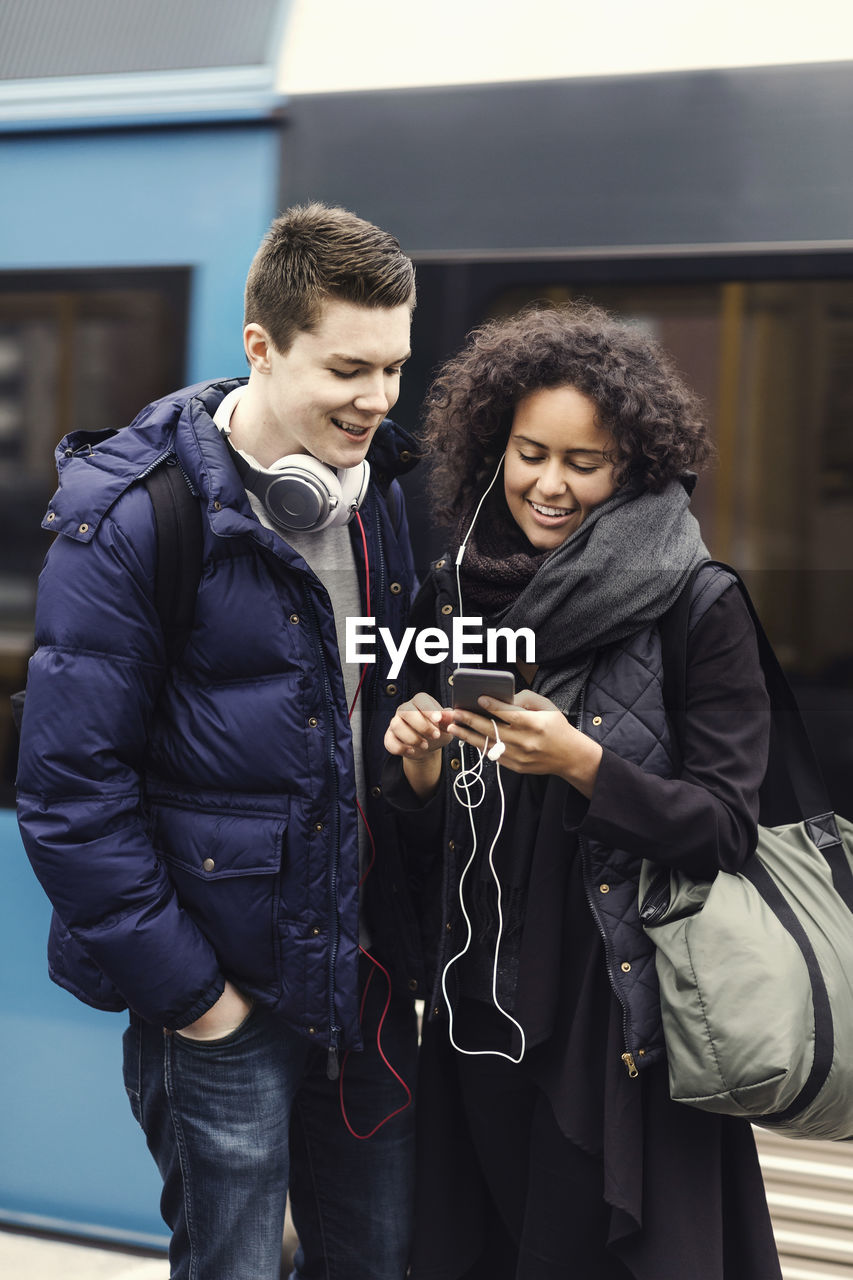 Multi-ethnic couple listening music through mobile phone on subway platform