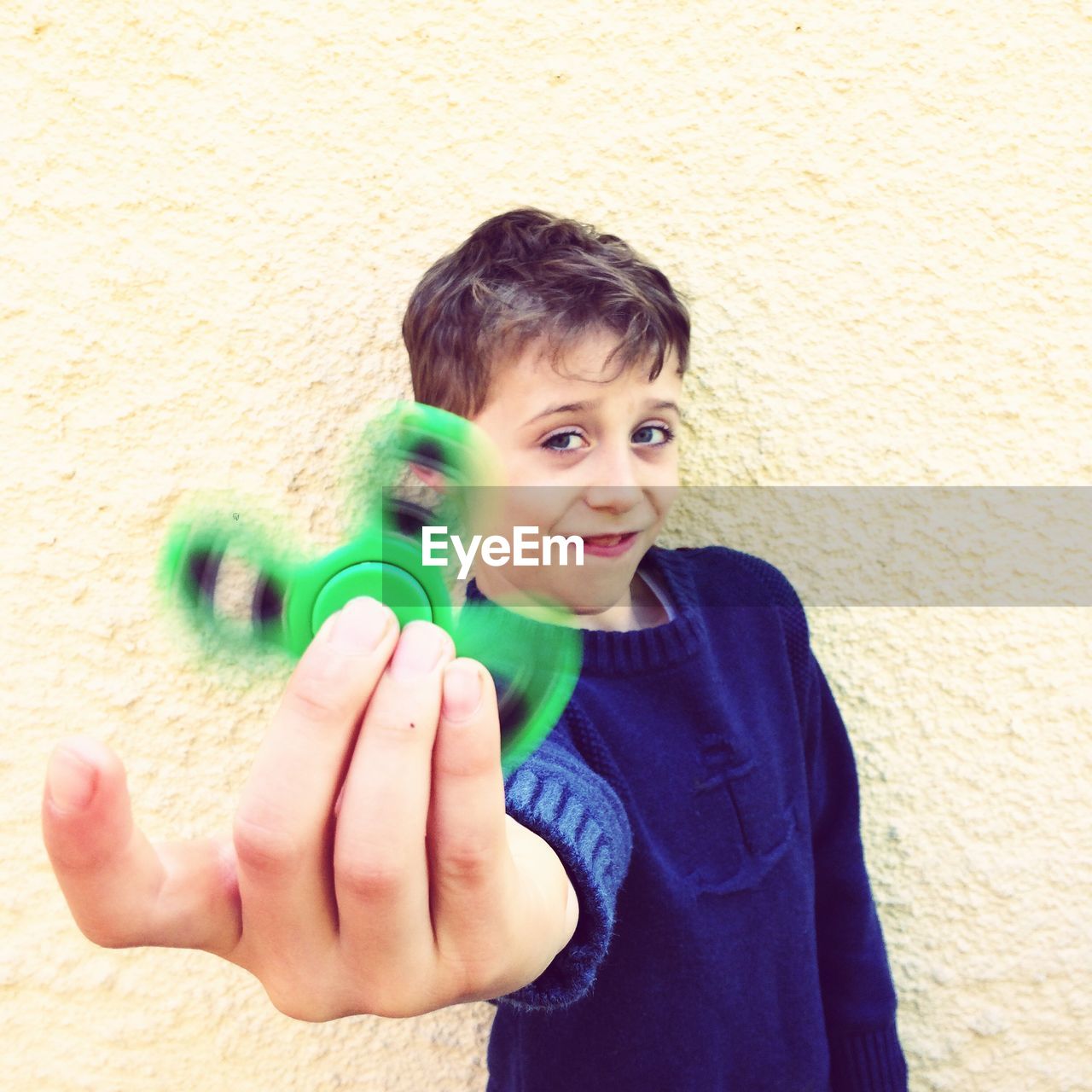 Portrait of boy playing with green fidget spinner against wall