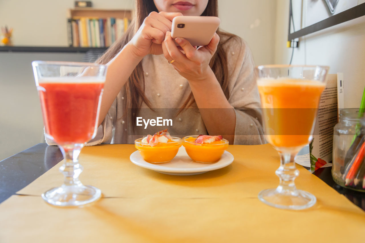 Midsection of woman photographing food through mobile phone at home