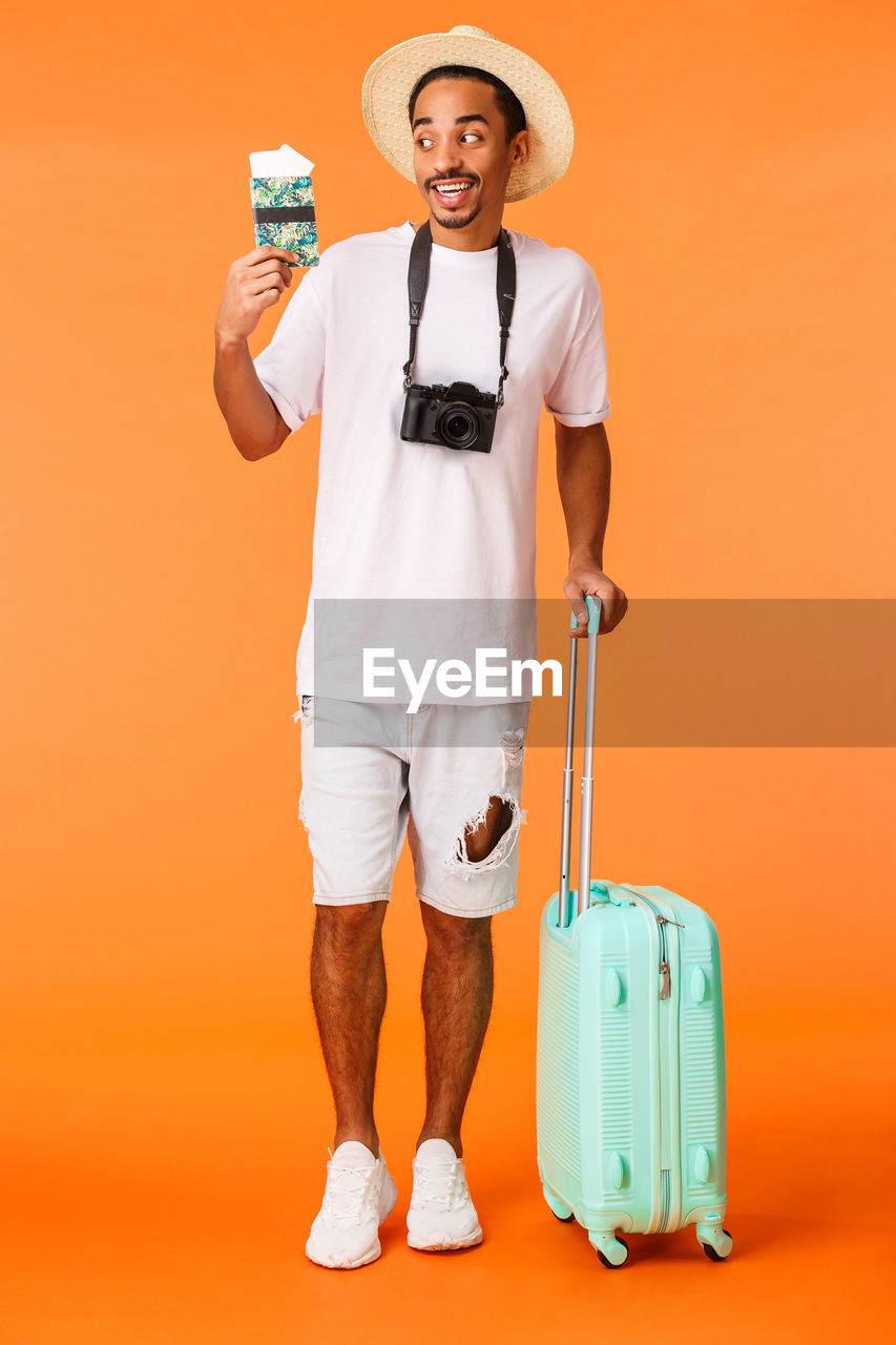 PORTRAIT OF SMILING MAN STANDING AGAINST ORANGE COLORED BACKGROUND