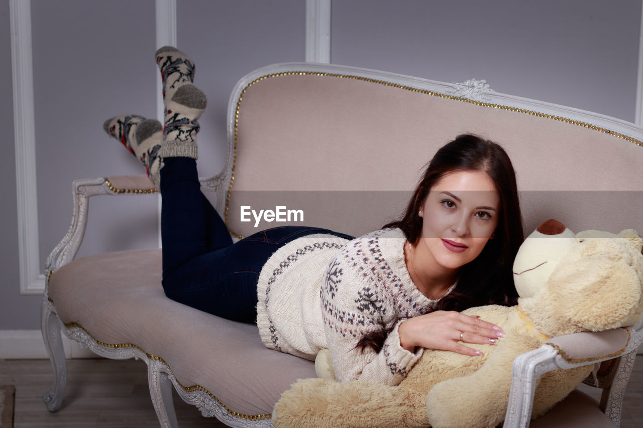 Portrait of young woman with teddy bear lying on sofa at home