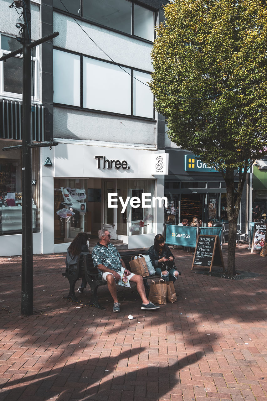 PEOPLE SITTING ON STREET AGAINST BUILDING