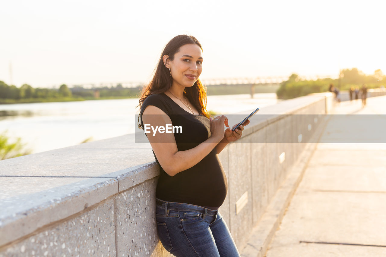 Portrait of young woman standing on mobile phone against sky