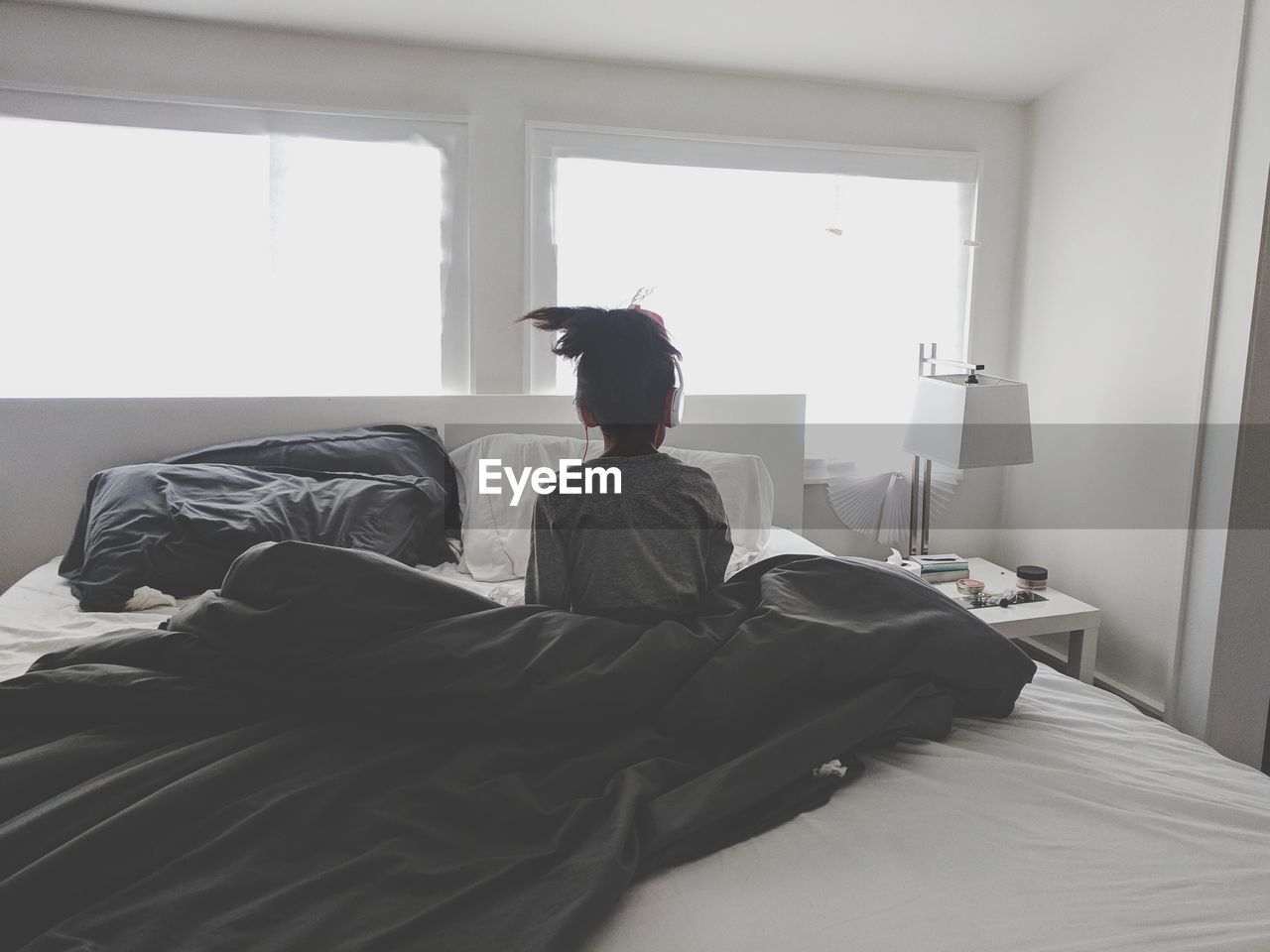 Rear view of girl sitting on bed at home