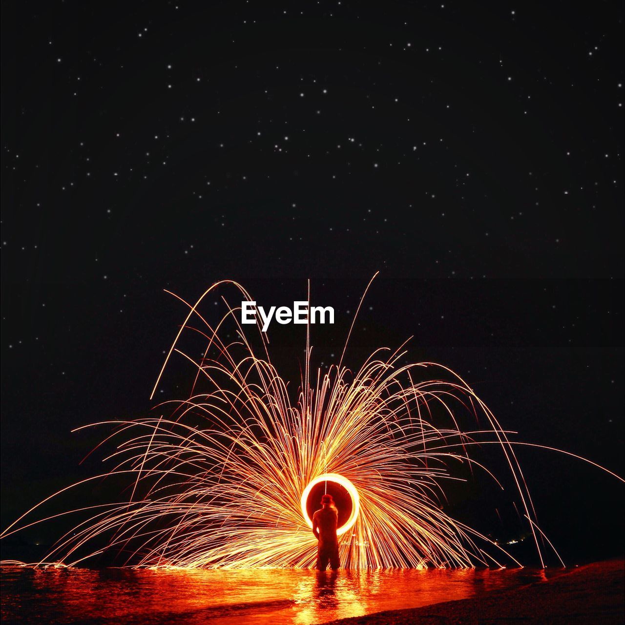 Rear view of man spinning wire wool against star field