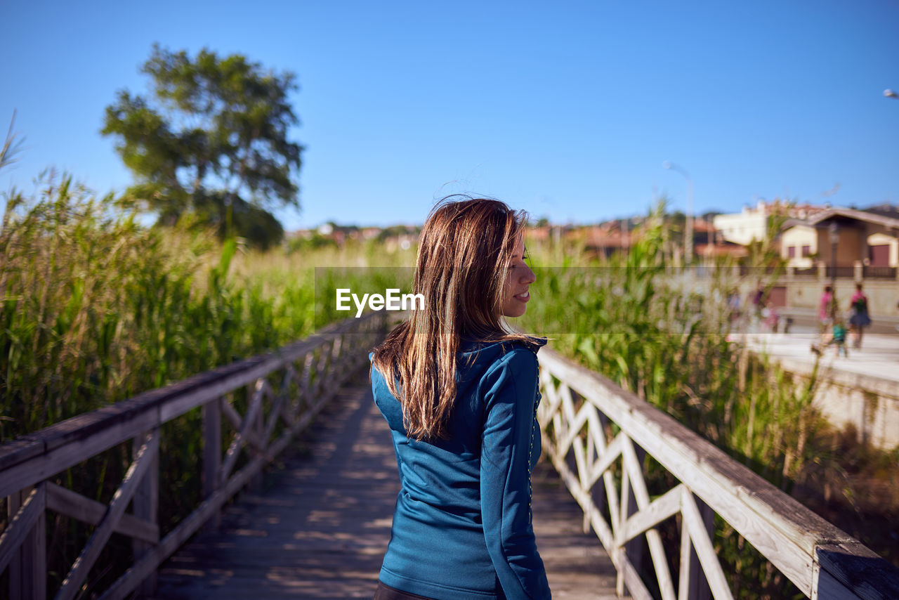 Rear view of woman walking on footbridge against clear blue sky
