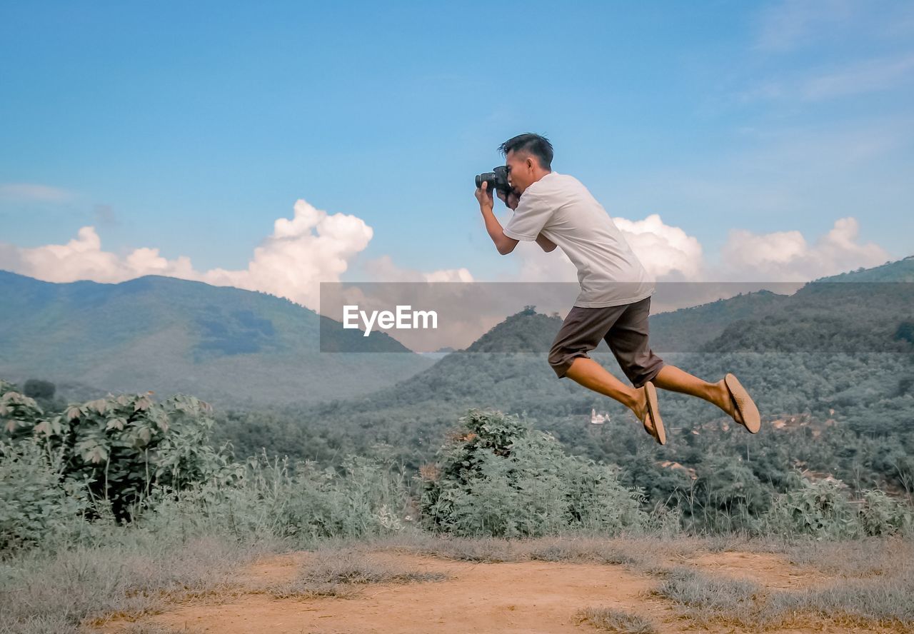 Side view of young man jumping in mountains against sky