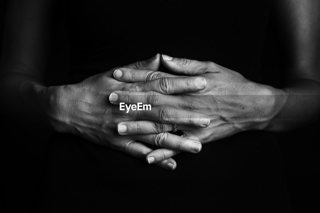 Close-up of hands clasped against black background