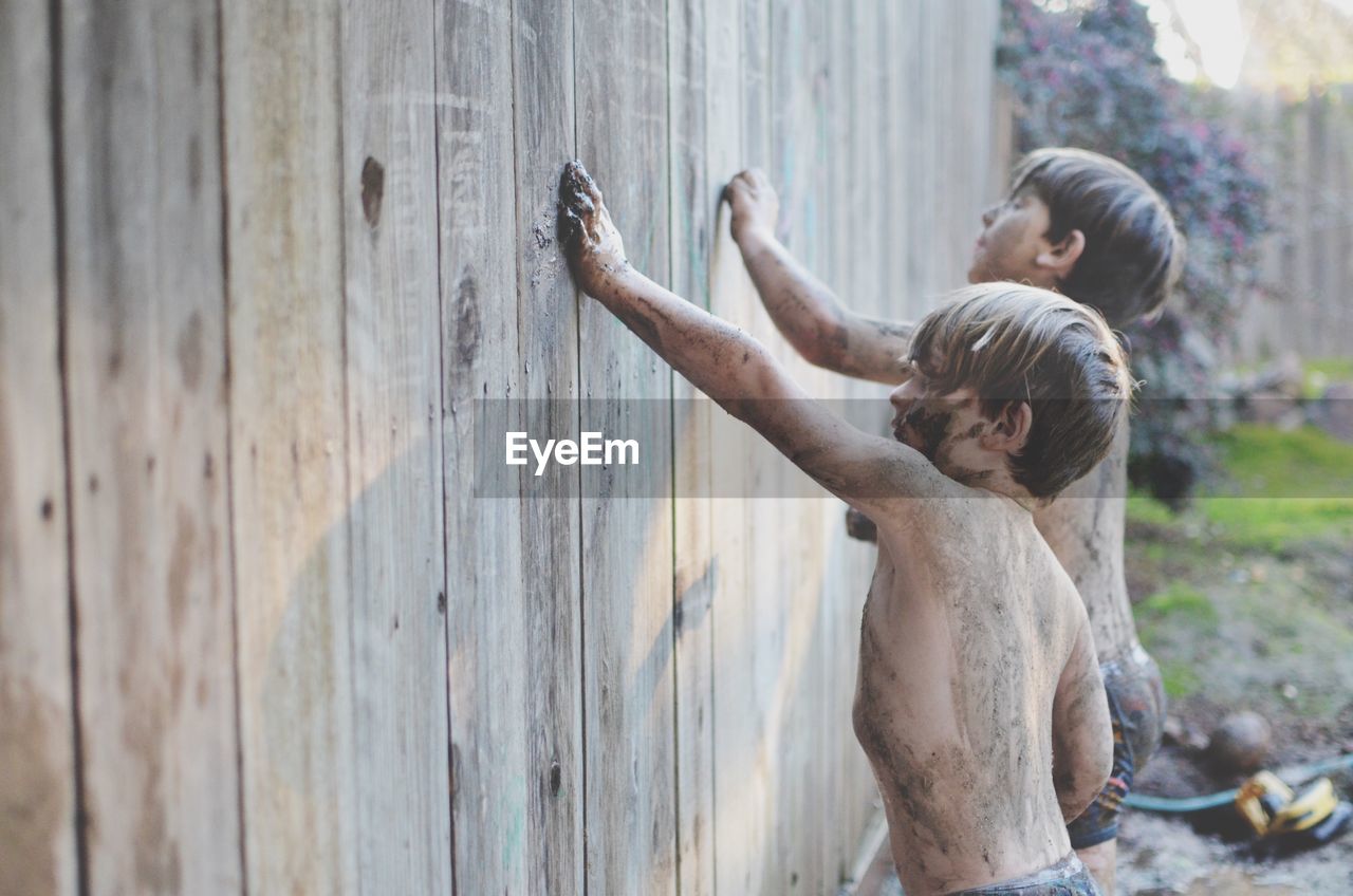 Dirty shirtless boys touching wooden wall