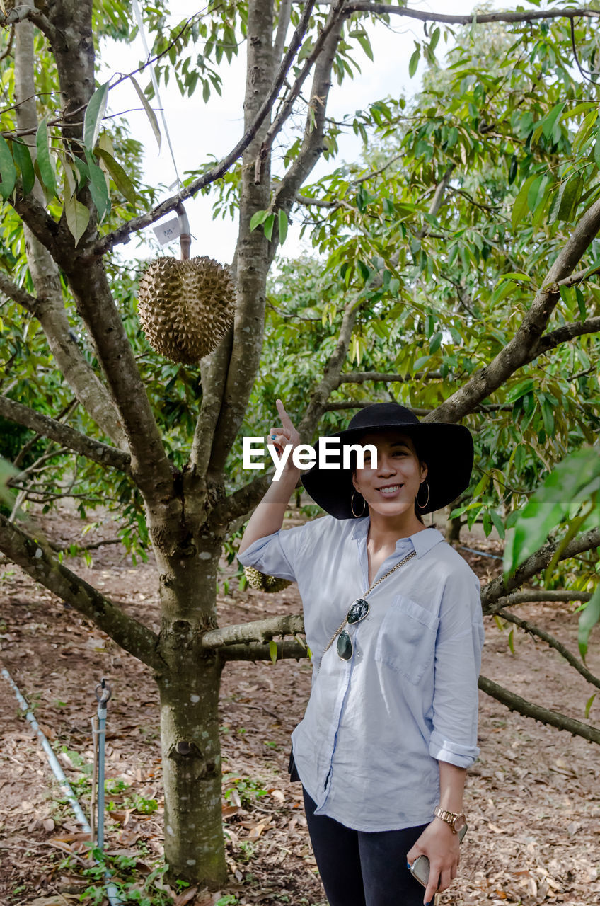 Smiling mid adult woman pointing at fruit while standing in forest