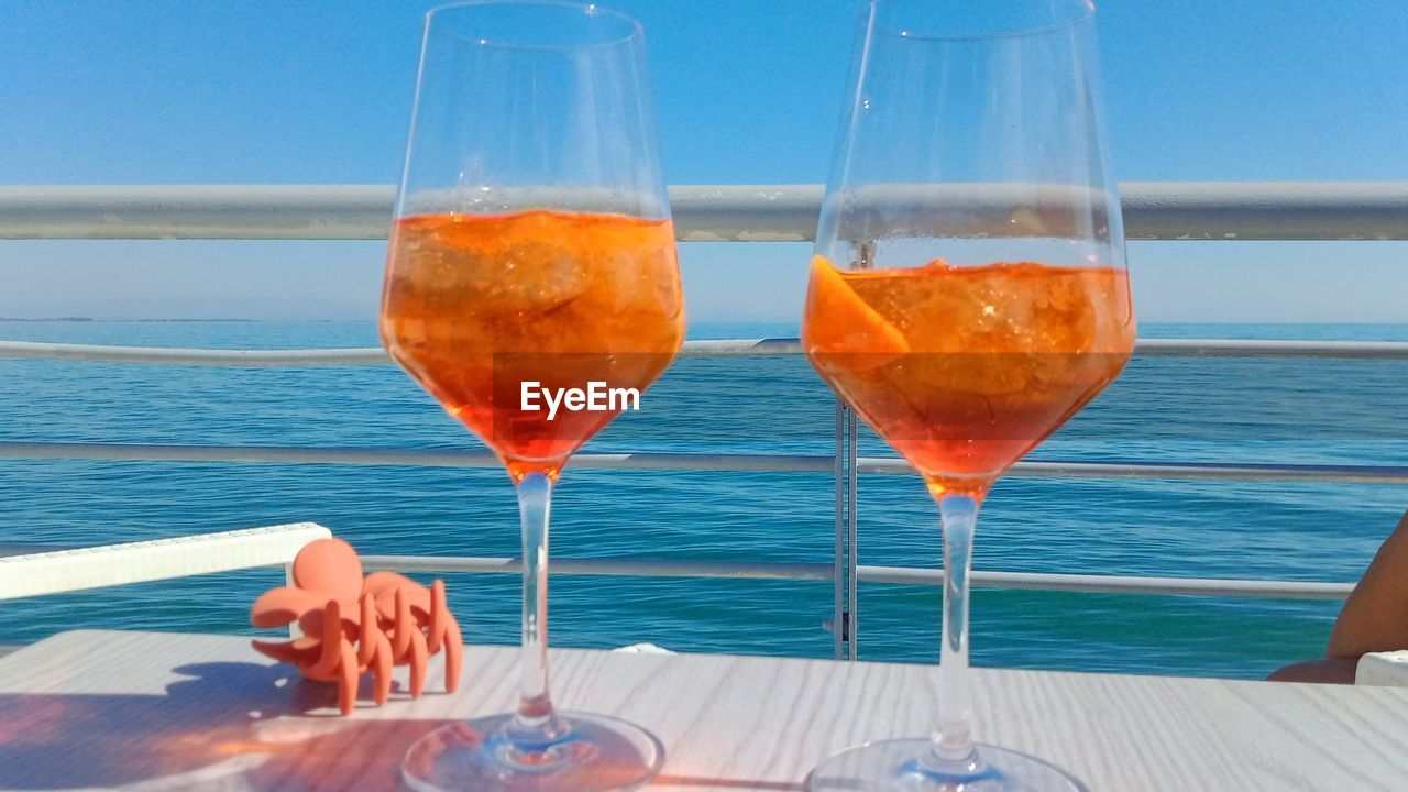 refreshment, drink, alcohol, food and drink, glass, water, wine, sea, sky, drinking glass, nature, household equipment, wine glass, cocktail, spritz, vacation, summer, alcoholic beverage, trip, food, horizon over water, land, soft drink, holiday, table, beach, day, no people, blue, sunlight, freshness, travel, horizon, relaxation, champagne flute, outdoors, champagne, stemware, rose wine, clear sky, travel destinations, beauty in nature