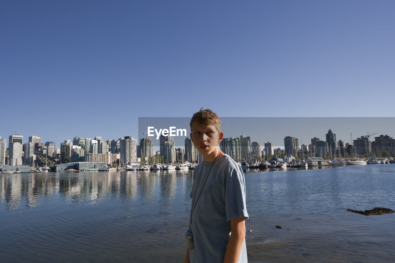 Teenage boy standing against buildings in city during sunny day