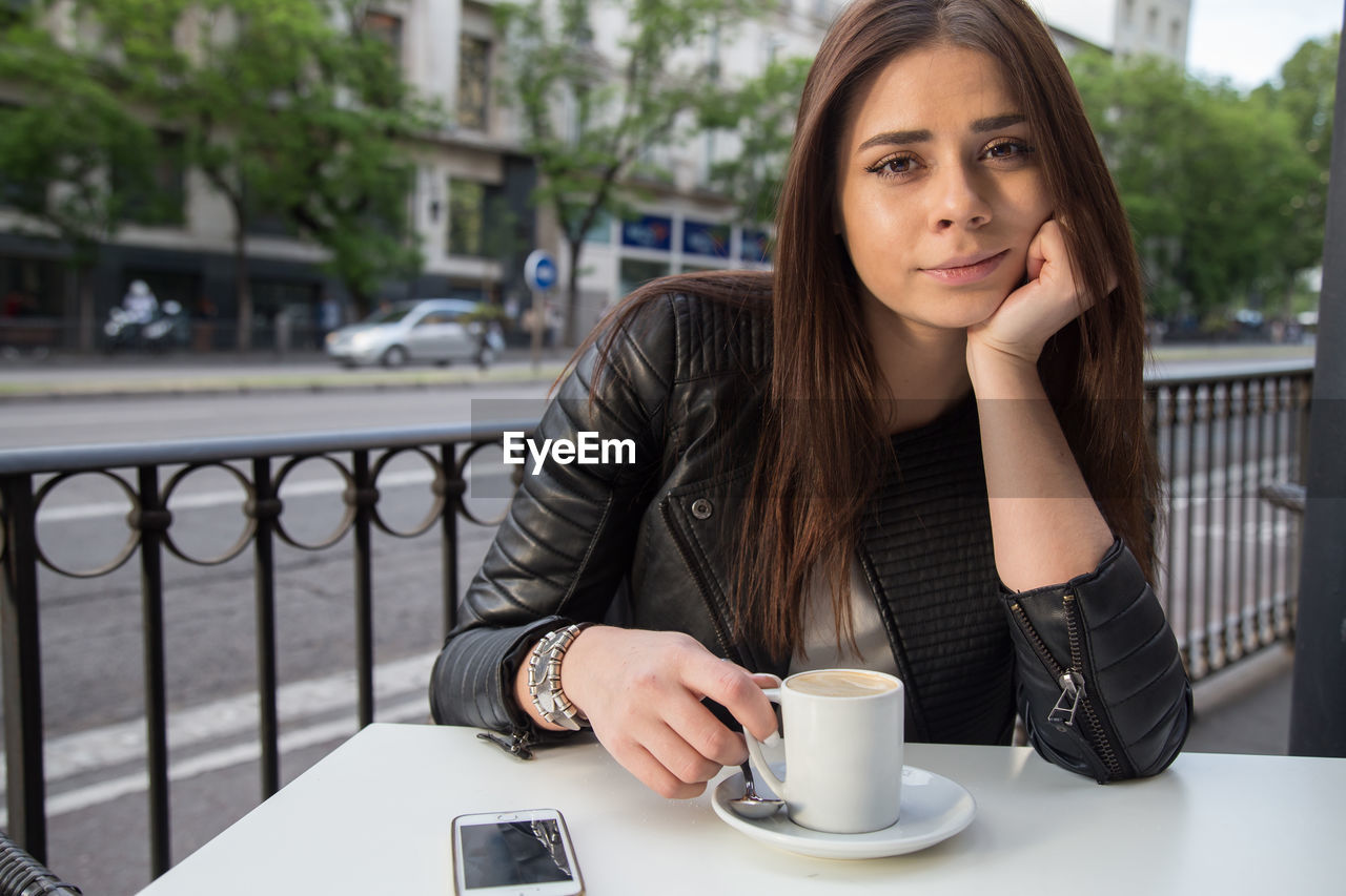 Portrait of young woman having coffee while sitting at sidewalk cafe