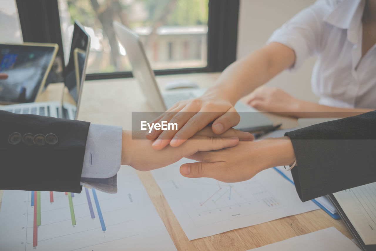 Cropped image of business colleagues huddling hands over table in office