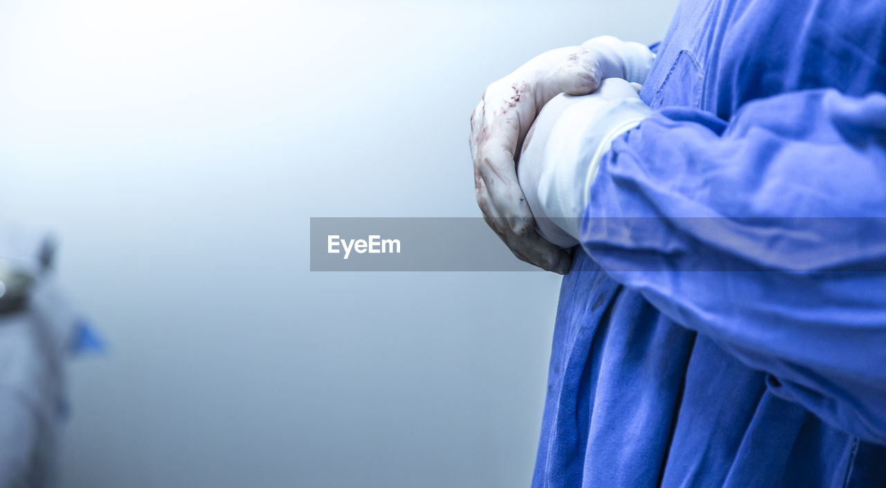 Midsection of surgeon wearing surgical gloves while standing against wall