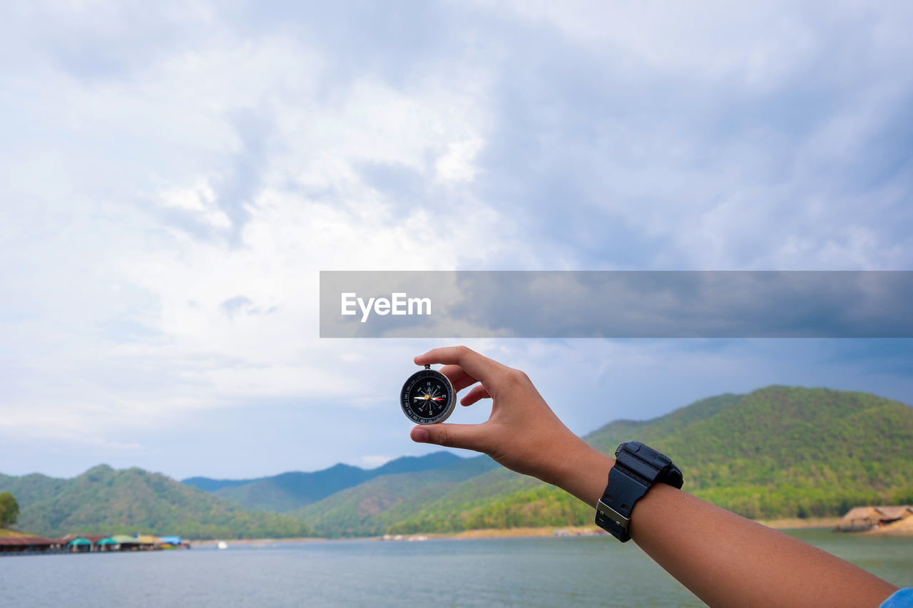 Cropped hand holding navigational compass by lake