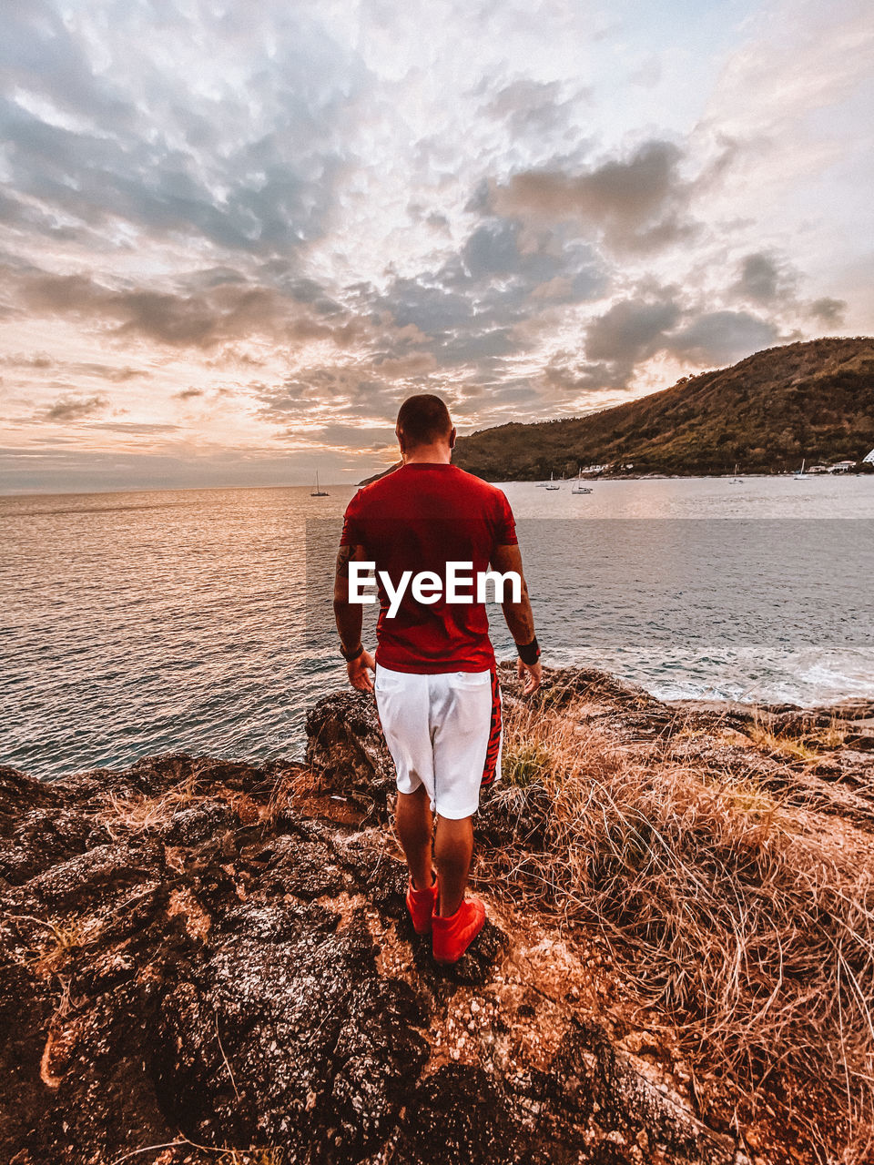 REAR VIEW OF MAN STANDING ON BEACH DURING SUNSET