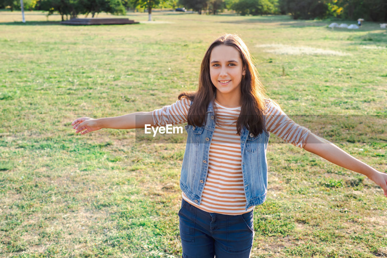 PORTRAIT OF SMILING YOUNG WOMAN STANDING IN FIELD