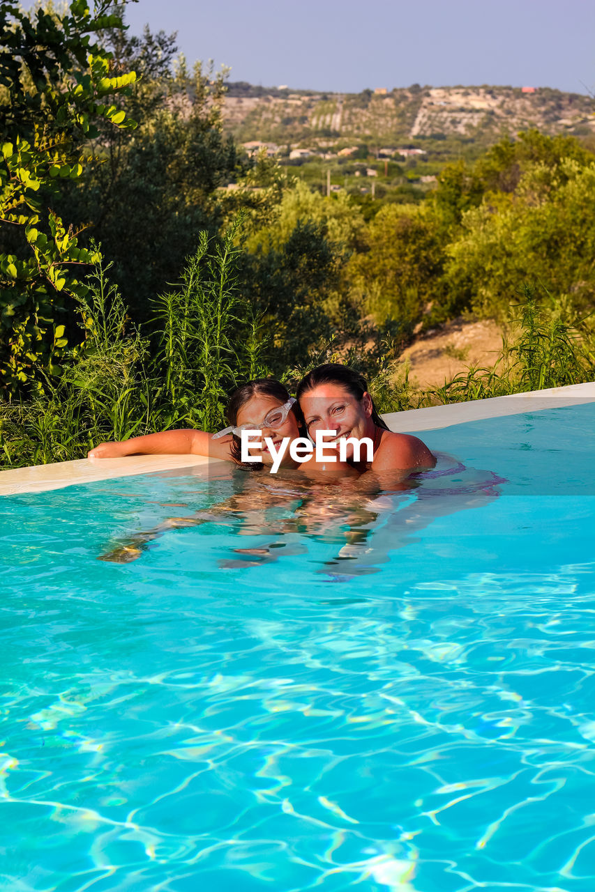 Portrait of smiling woman and daughter enjoying in swimming pool on sunny day